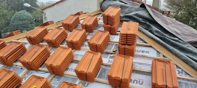 Écran sous-toiture et liteaux posés, tuiles neuves réparties en piles sur la couverture